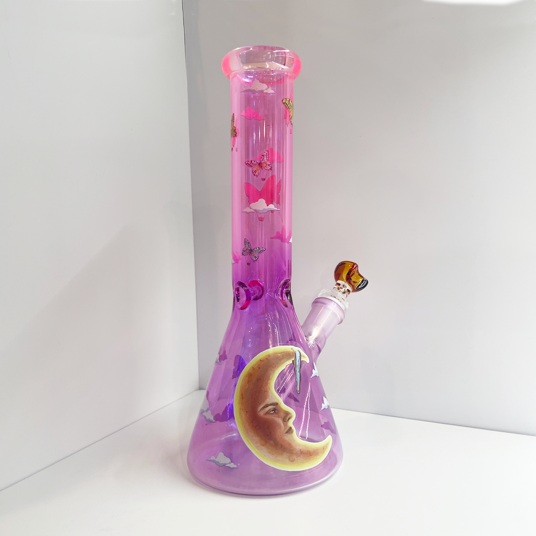 10 inch beaker bong with light purple base that transitions to bright pink at top with large celestial moon, butterflies and cloud decals bliss shop chicago