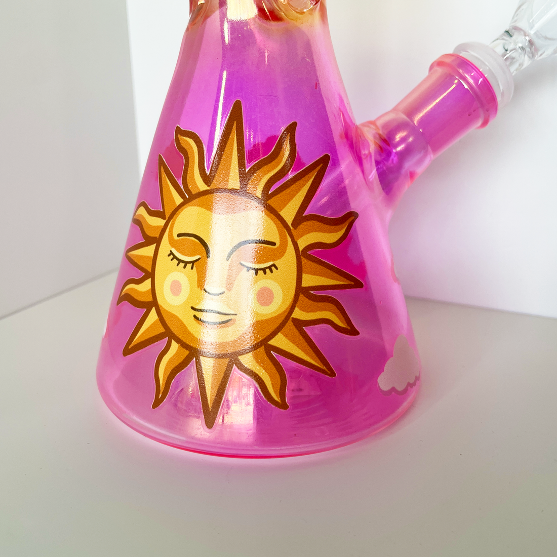 10 inch beaker bong with a bright pink base that transitions to yellow gold at top with large celestial sun, butterflies and cloud decals bliss shop chicago